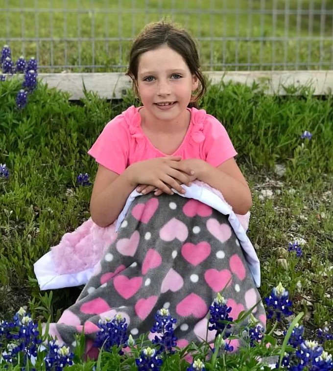 A girl in a Texas bluebonnet field holding a handmade blanket